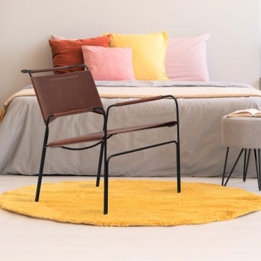 Yellow round rug and stool in front of grey bed with pillows in bedroom interior with poster. Real photo